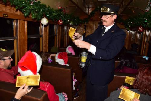 A train conductor hands out tickets to passengers wearing festive hats inside a decorated train car.