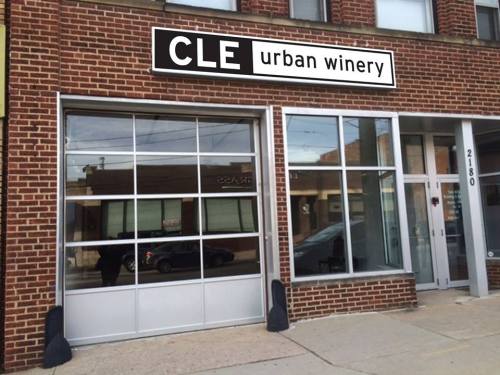 Exterior of CLE Urban Winery, featuring a large glass window and a sign above the entrance on a brick building.