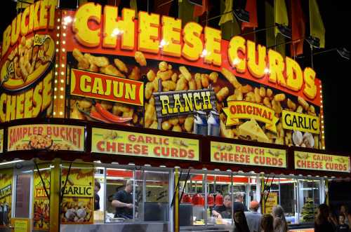 Brightly lit food stand featuring a large sign for cheese curds with various flavors like Cajun, ranch, and garlic.