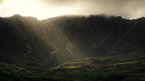 Sunlight breaks through clouds over a lush, green mountain landscape, creating a dramatic and serene atmosphere.