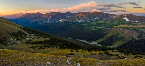 A panoramic view of mountains at sunset, with lush valleys and forests under a colorful sky.