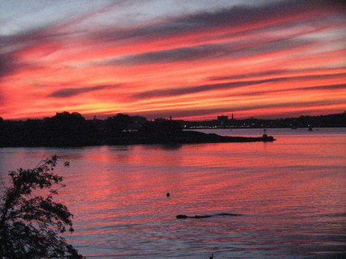 A vibrant sunset over a calm water body, with colorful clouds reflecting shades of orange, pink, and purple.