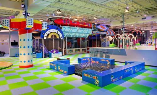 Brightly colored indoor play area with climbing structures, slides, and soft flooring in a spacious environment.