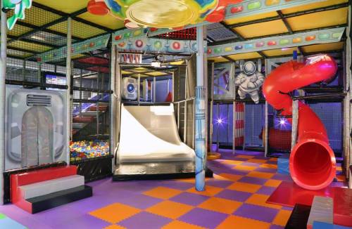 Colorful indoor play area featuring a slide, a red tube slide, and ball pit with soft flooring.