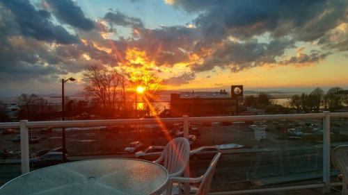 A vibrant sunset over a lake, with clouds and silhouettes of trees, viewed from a balcony with a table and chairs.