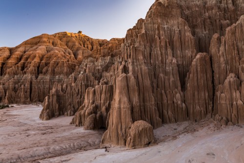 Rocky formations with tall, jagged cliffs and warm earthy tones under a clear blue sky.