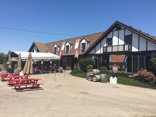 A rustic building with a sloped roof, outdoor seating, and flower beds on a sunny day.