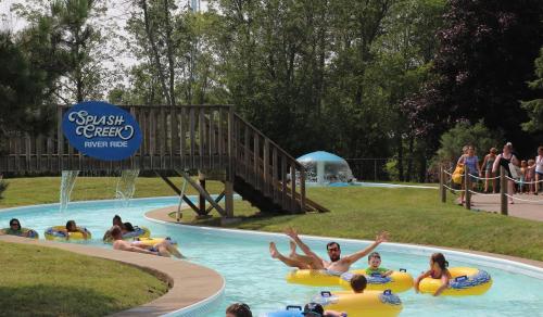 People enjoying a lazy river ride on inflatable tubes at Splash Creek, surrounded by greenery and a wooden bridge.