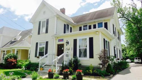 A charming yellow house with black shutters, a welcoming entrance, and flower pots in front, set against a blue sky.