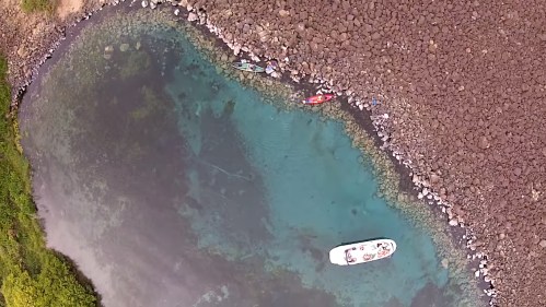 Aerial view of a turquoise water body with rocky shores and a small boat anchored nearby.
