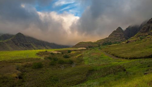 Lush green landscape with rolling hills and mountains under a cloudy sky.