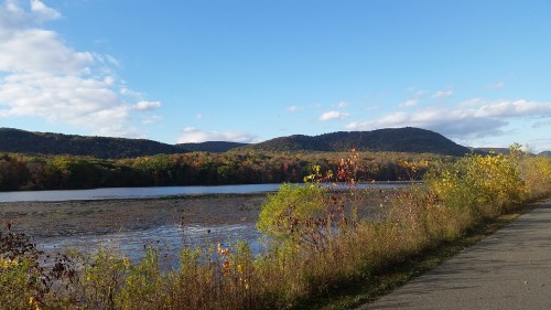 Scenic view of a river bordered by colorful autumn foliage and rolling hills under a clear blue sky.