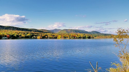 A serene lake surrounded by colorful autumn trees and distant mountains under a clear blue sky.