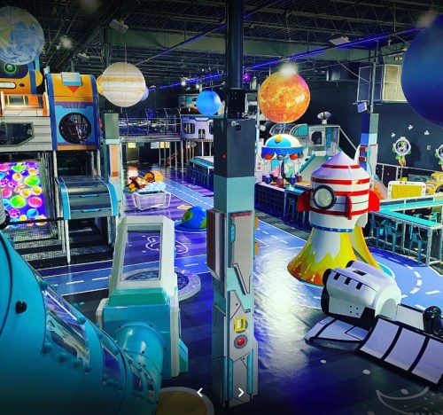 Colorful indoor play area featuring space-themed structures, planets, and interactive games for children.