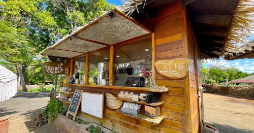 A wooden food kiosk with a thatched roof, featuring a menu board and signs for pickup and free treats.
