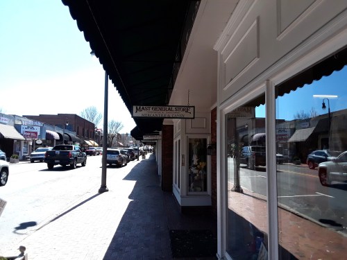 A sunny street view featuring the Mast General Store sign and storefronts along a bustling sidewalk.