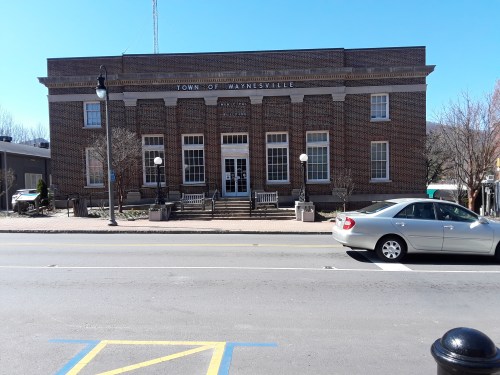 Historic brick building with "Town of Waynesville" sign, benches, and street view on a clear day.