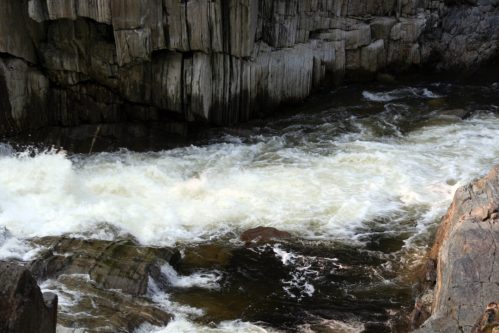 Rushing water flows over rocky terrain, surrounded by steep, textured cliffs.