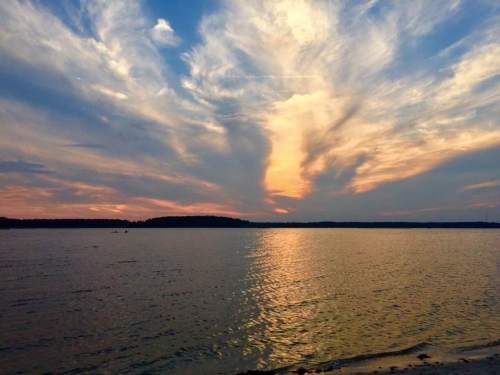 A serene sunset over a calm lake, with vibrant clouds reflecting on the water's surface.