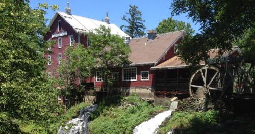 A red historic mill surrounded by lush greenery and a small waterfall, with a large water wheel visible.