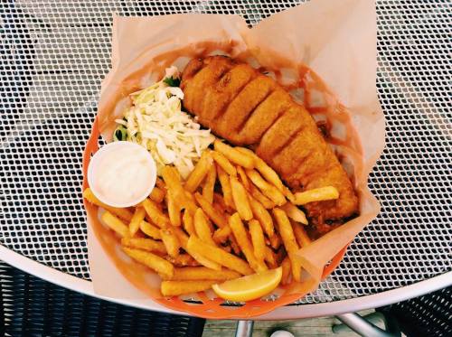A plate of fried fish with coleslaw, fries, and a side of dipping sauce, served on a paper-lined basket.