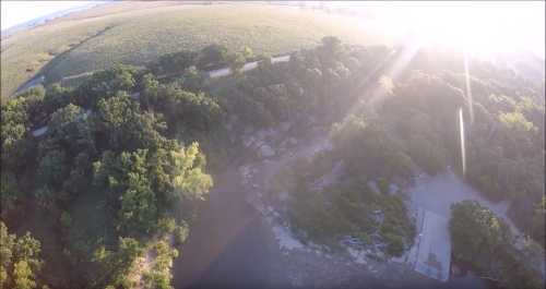 Aerial view of a lush green landscape with a riverbank and sunlight shining through trees.