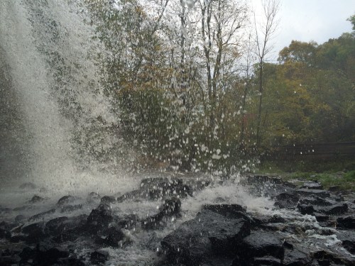 Water cascades over rocks, creating a misty spray in a lush, green forest setting.