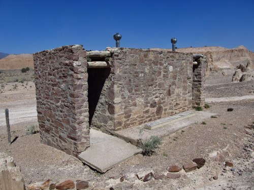 A small, weathered stone structure in a desert landscape under a clear blue sky.