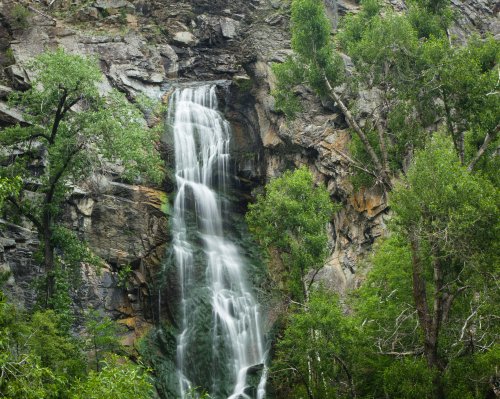 A cascading waterfall flows down rocky cliffs, surrounded by lush green trees and foliage.