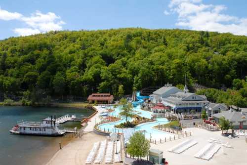 A scenic view of a water park by a lake, surrounded by lush green hills and a clear blue sky.