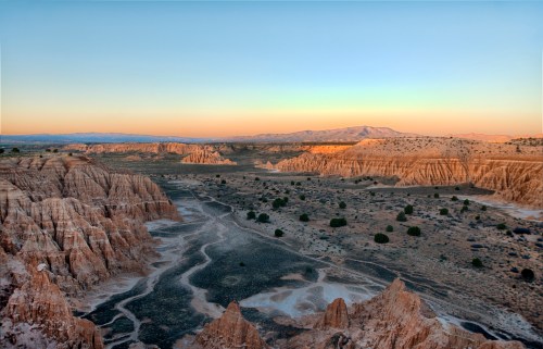A panoramic view of rugged, colorful rock formations and a vast landscape under a clear sky at sunset.