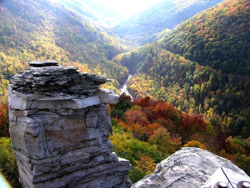 A rocky outcrop overlooks a vibrant valley filled with autumn foliage and a winding river below.