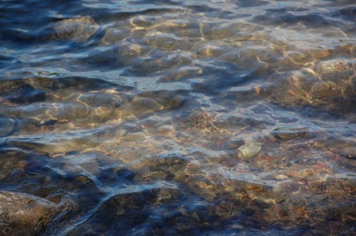 Clear water gently rippling over colorful pebbles and rocks beneath the surface.
