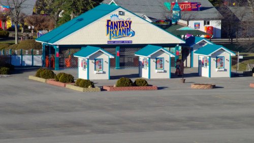 Entrance to Fantasy Island amusement park, featuring a colorful building and ticket booths, surrounded by greenery.