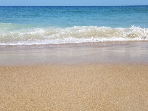A serene beach scene with gentle waves lapping at the sandy shore under a clear blue sky.
