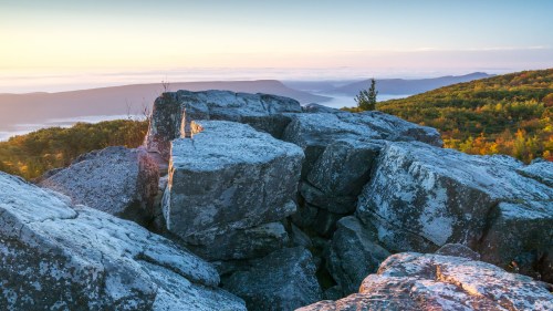 Sunrise over rocky outcrops with lush green hills and misty valleys in the background.