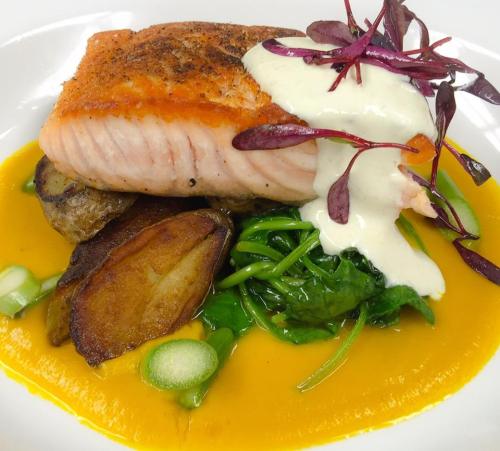 A plated dish featuring salmon on a bed of spinach, with roasted potatoes and a creamy sauce, garnished with microgreens.