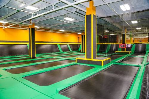 Indoor trampoline park featuring multiple trampolines with green and black surfaces and bright orange walls.