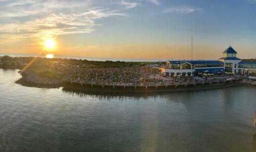 A vibrant sunset over a crowded waterfront venue, reflecting on calm waters.
