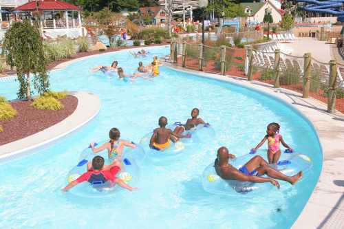 A group of people floating on inner tubes in a lazy river at a water park, surrounded by greenery and lounge chairs.