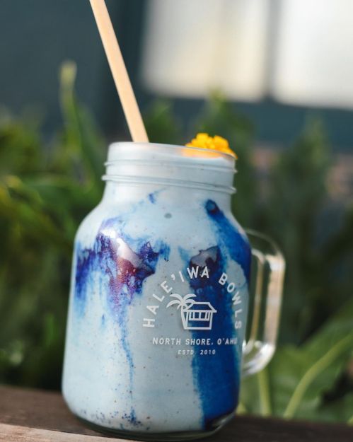 A colorful smoothie in a mason jar with a straw, featuring blue and purple swirls, set against a green background.