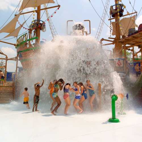 Children and adults enjoy a water play area with a large splash feature, surrounded by pirate-themed decorations.