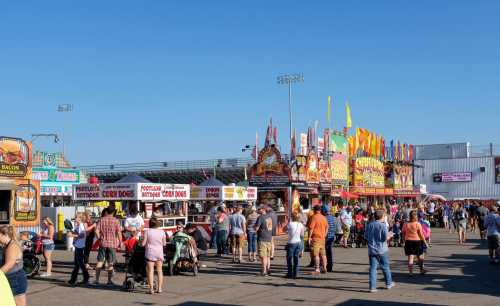 A bustling fairground with food stalls, colorful flags, and crowds enjoying a sunny day.