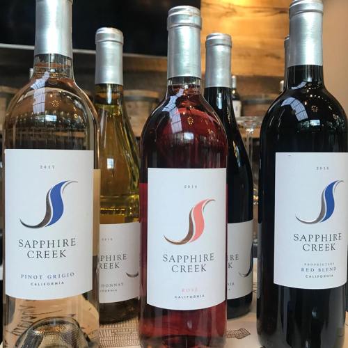A selection of Sapphire Creek wine bottles, including Pinot Grigio, Chardonnay, and Red Blend, displayed on a table.