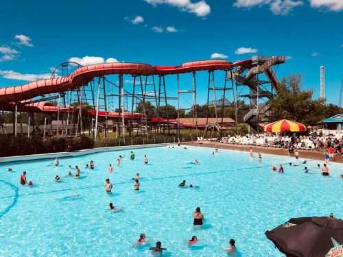 A vibrant water park scene with a large pool, water slides, and people enjoying the sun and swimming.