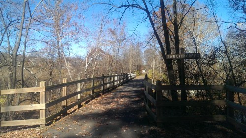 A path leads to a sign for Two Lick Creek, surrounded by trees and autumn foliage under a clear blue sky.