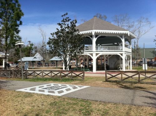 A white gazebo with a gray roof surrounded by trees and picnic areas in a park setting.