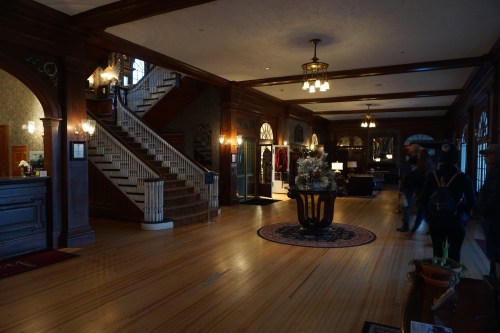 A spacious, elegant lobby with wooden accents, a staircase, and cozy seating areas, illuminated by warm lighting.