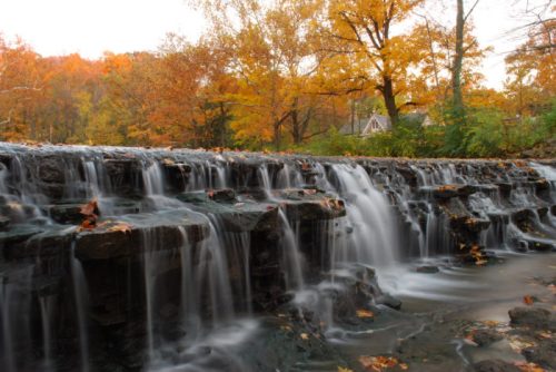 A serene waterfall cascades over rocky ledges, surrounded by vibrant autumn foliage.