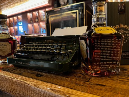 A vintage Corona typewriter next to a bottle of Jack Daniel's whiskey on a wooden bar.
